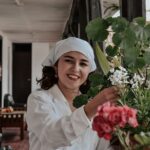 A smiling woman arranges flowers indoors in Chachapoyas, Peru, adding beauty to the space.