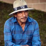 Candid outdoor portrait of a man in a blue shirt and straw hat sitting casually in Santa Maria, CA.