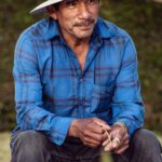 Candid outdoor portrait of a man in a blue shirt and straw hat sitting casually in Santa Maria, CA.