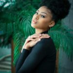 Stylish woman with natural curly hair in a lush indoor setting.